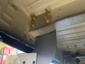 Close-up of a vehicle's undercarriage with gold-colored bolts and a white foam block.